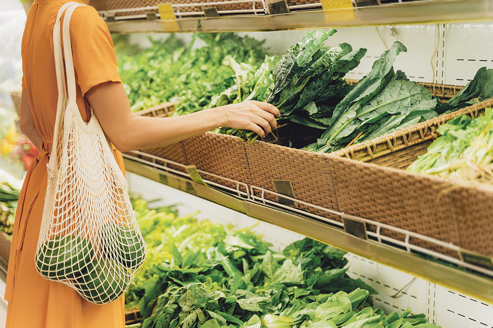 Frau in einem Supermarkt greift zu grünem Gemüse.