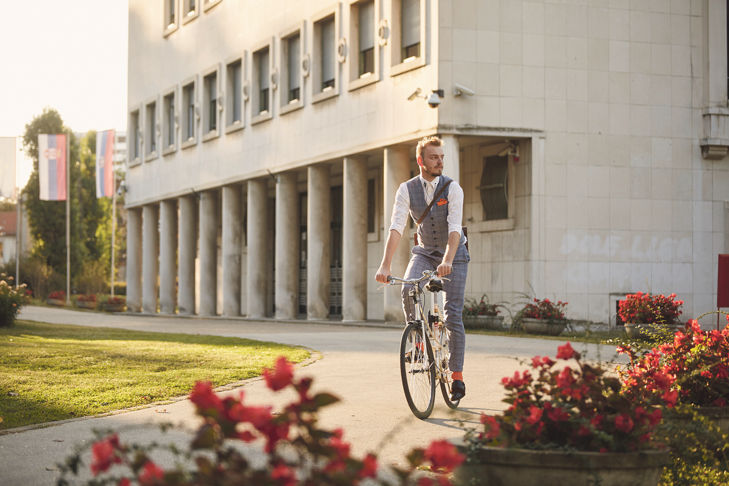 Ein Mann im Anzug fährt vor einem Gebäude Fahrrad.