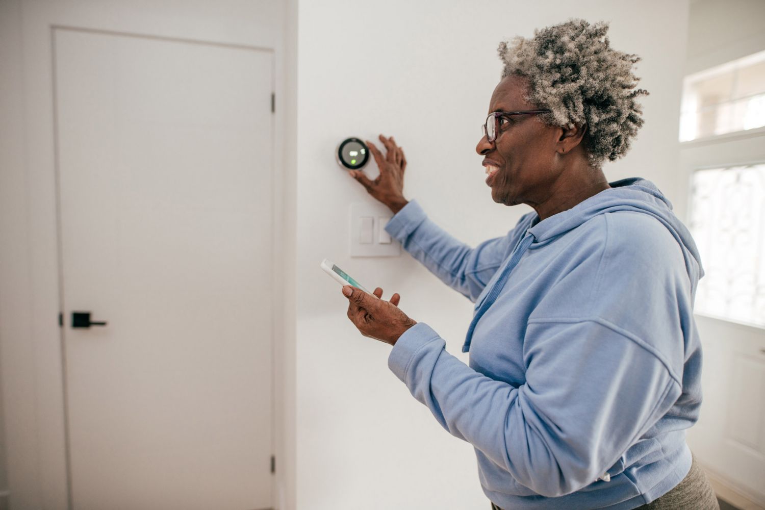 Eine ältere Dame bedient per Handy ihr Smart-Home-Thermostat.