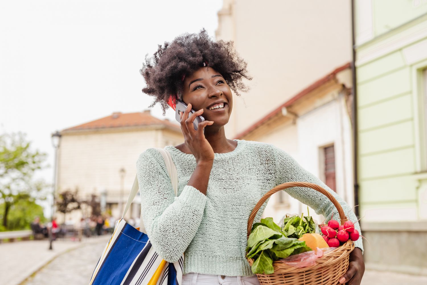 Eine Frau trägt einen Korb mit frischen Lebensmitteln, während sie telefoniert. 